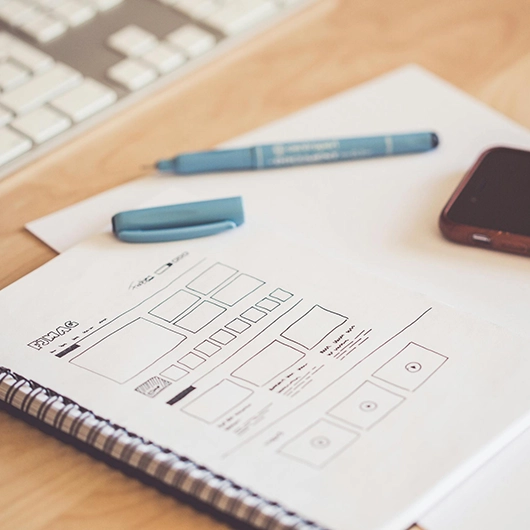 Arbeitsplatz mit Block und Stift auf dem eine Webseitenstruktur aufgemalt ist für ein Webdesign